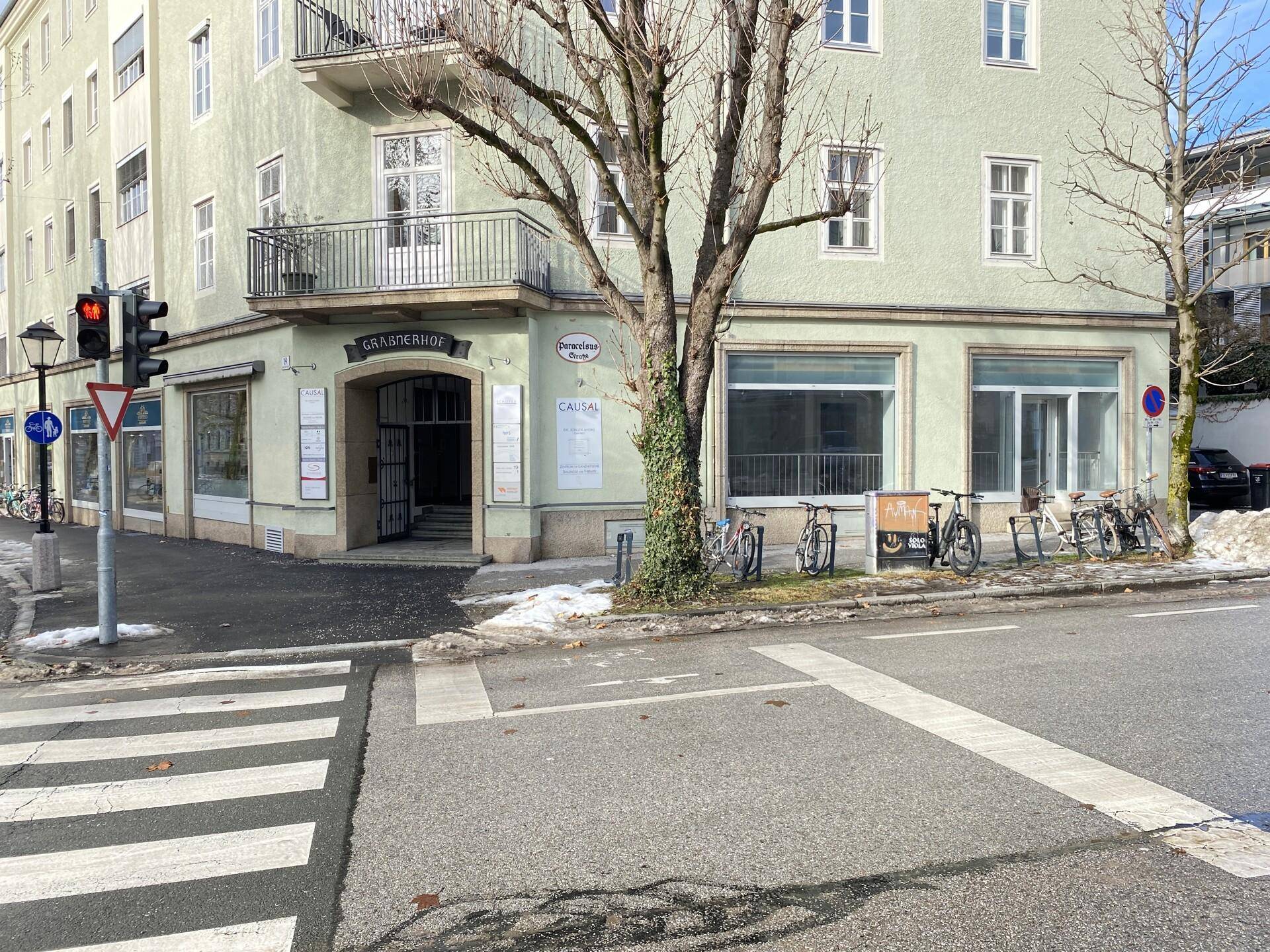 Eckgebäude an einer belebten Kreuzung mit Geschäften im Erdgeschoss und Fußgängerüberweg.
