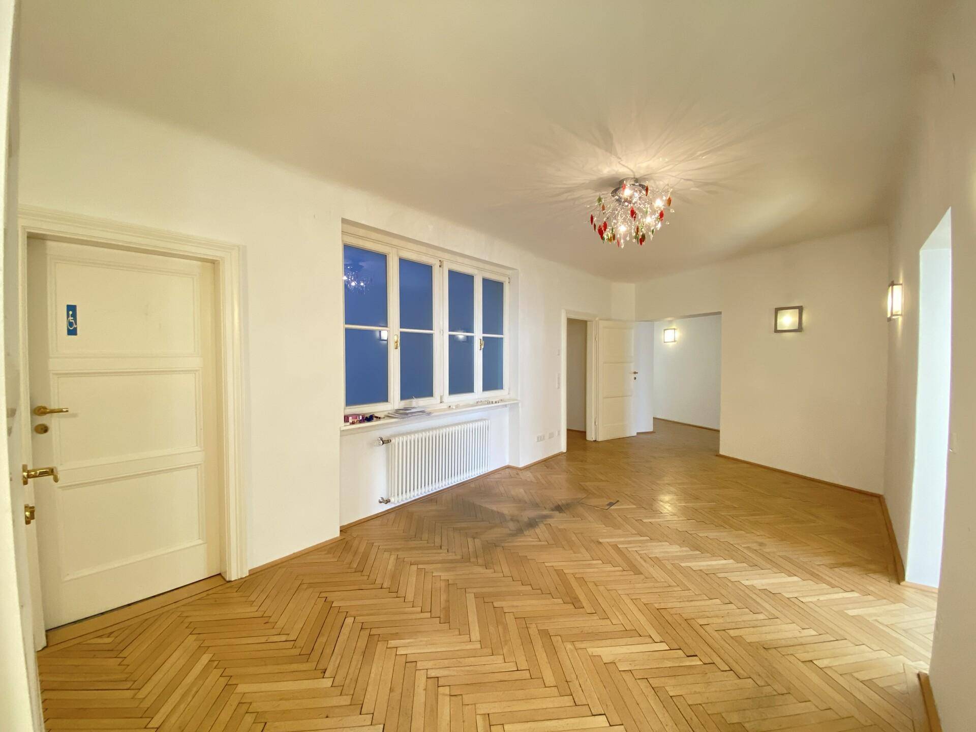 Langer Flur mit Holzparkett, großen Fenstern und einer auffälligen Deckenleuchte, die den Raum erhellt.