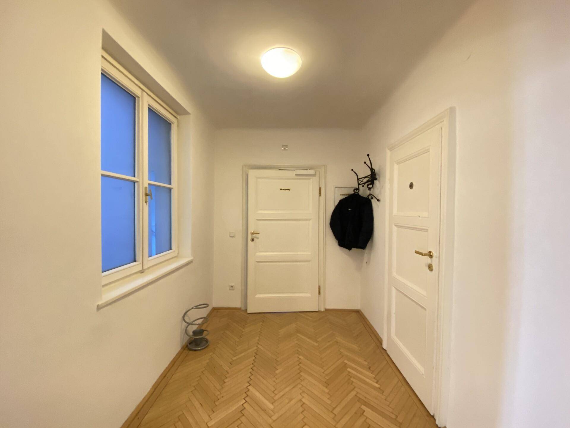 Eingangsbereich mit Fischgrätparkett, Fenster und Garderobe, der zu weiteren Räumen führt.