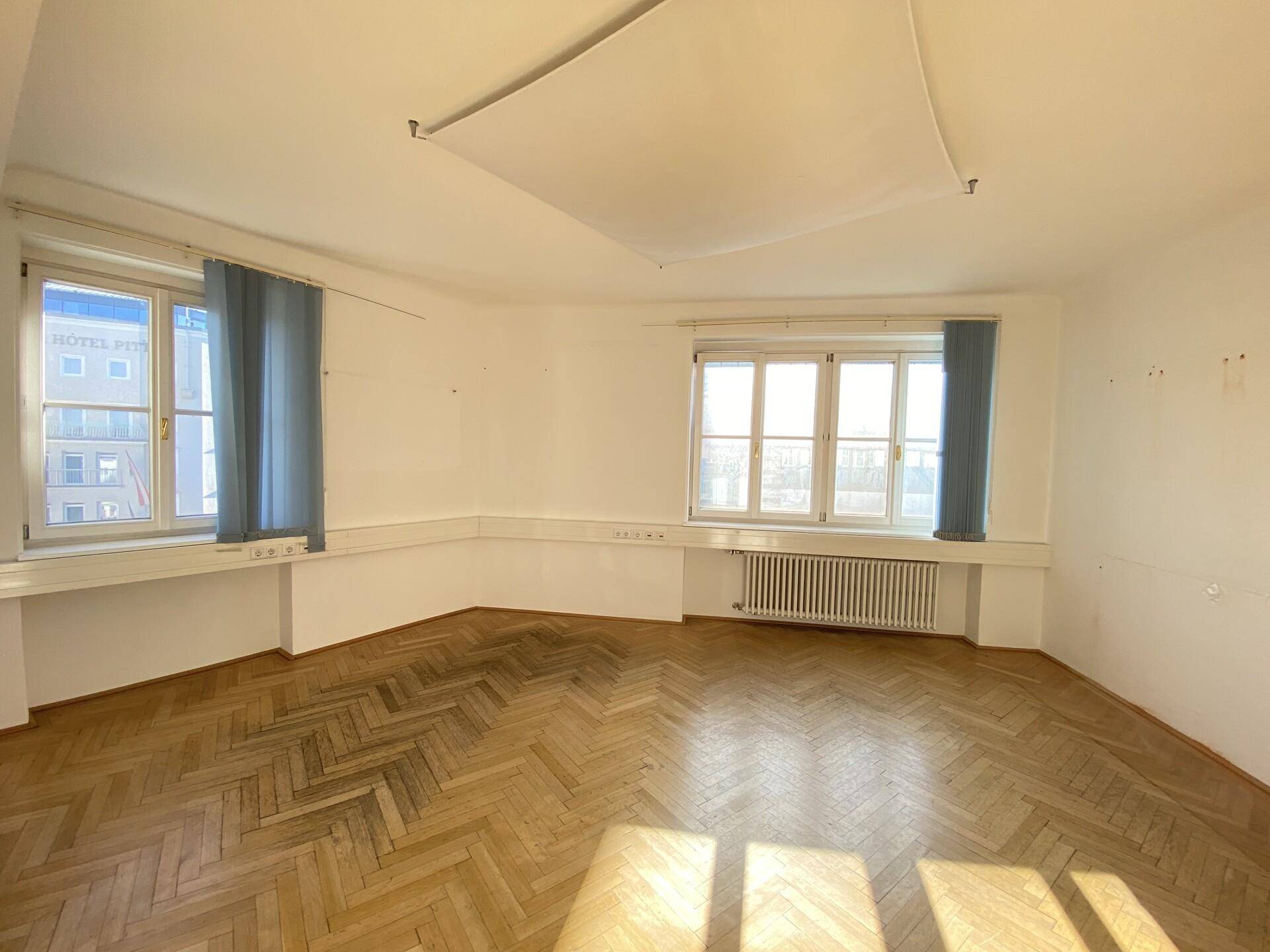 Geräumiger Büroraum mit Holzparkett und Blick auf die umliegenden Gebäude durch die Fenster.