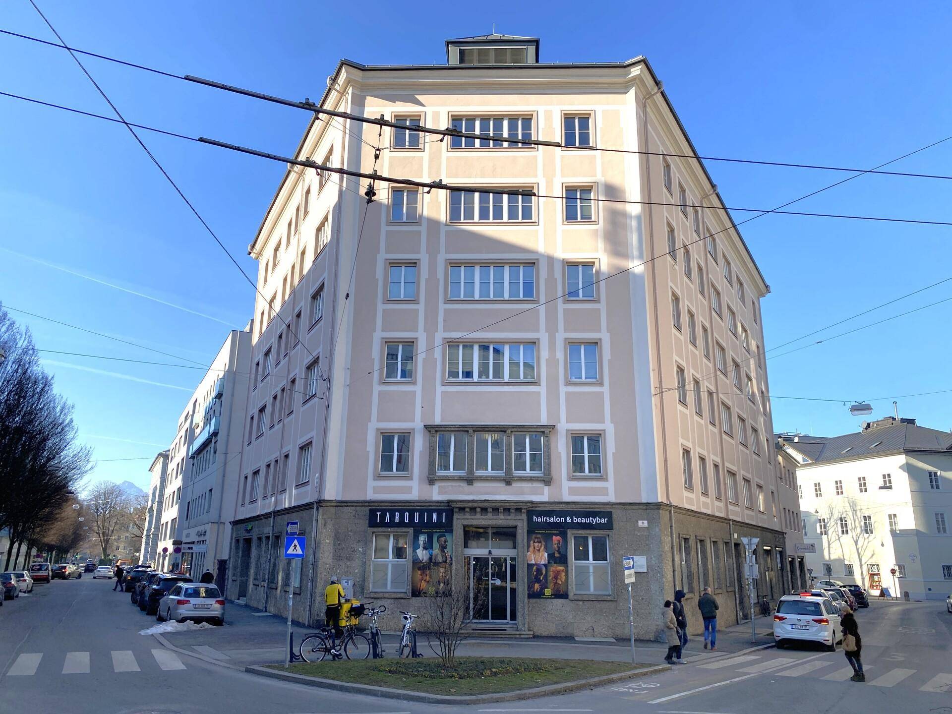 Mehrstöckiges Eckgebäude mit klassischer Architektur, Geschäften im Erdgeschoss und Blick auf die Stadtstraße.