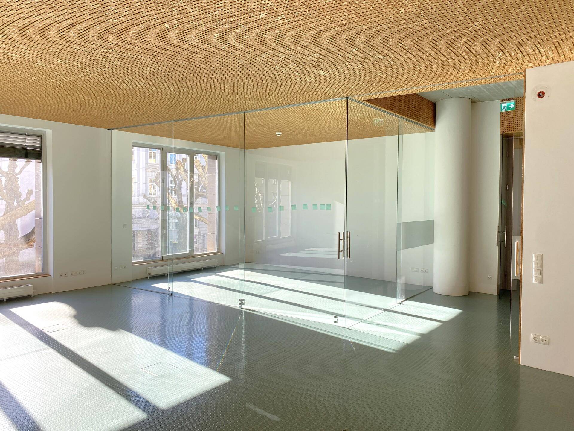 Offener Bürobereich mit raumhohen Glaswänden, die separate Arbeitsbereiche schaffen, und einer Holzdecke.