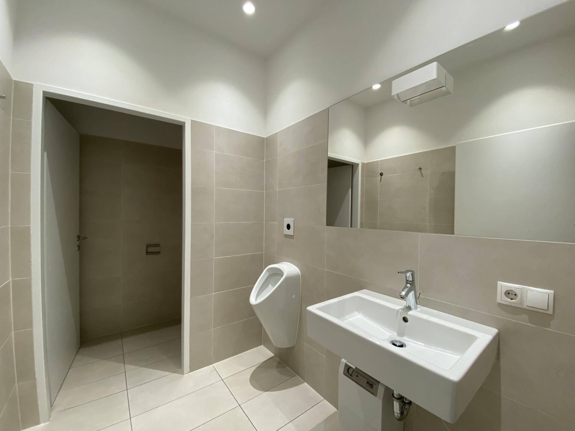 Modernes Badezimmer mit beigefarbenen Fliesen, Waschbecken und einem Urinal.