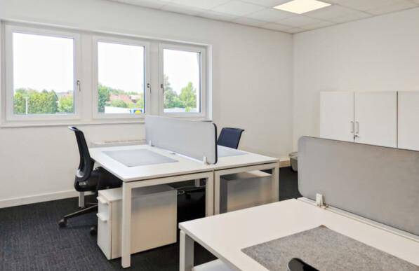 Helles Büro mit mehreren Arbeitsplätzen, großen Fenstern und Blick ins Grüne.