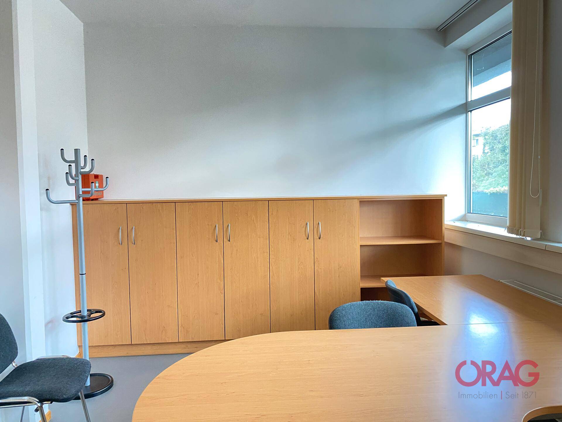 Detailansicht eines Büroraums mit Holzschränken, einem Schreibtisch und einem Garderobenständer.