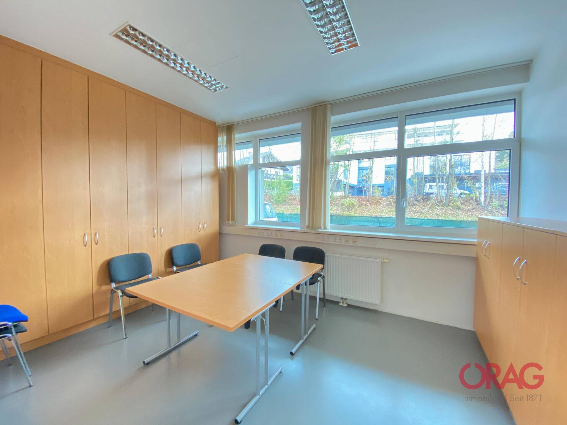 Geräumiger Büroraum, eingerichtet als Besprechungszimmer mit Tisch und Stühlen, umgeben von Holzschränken.