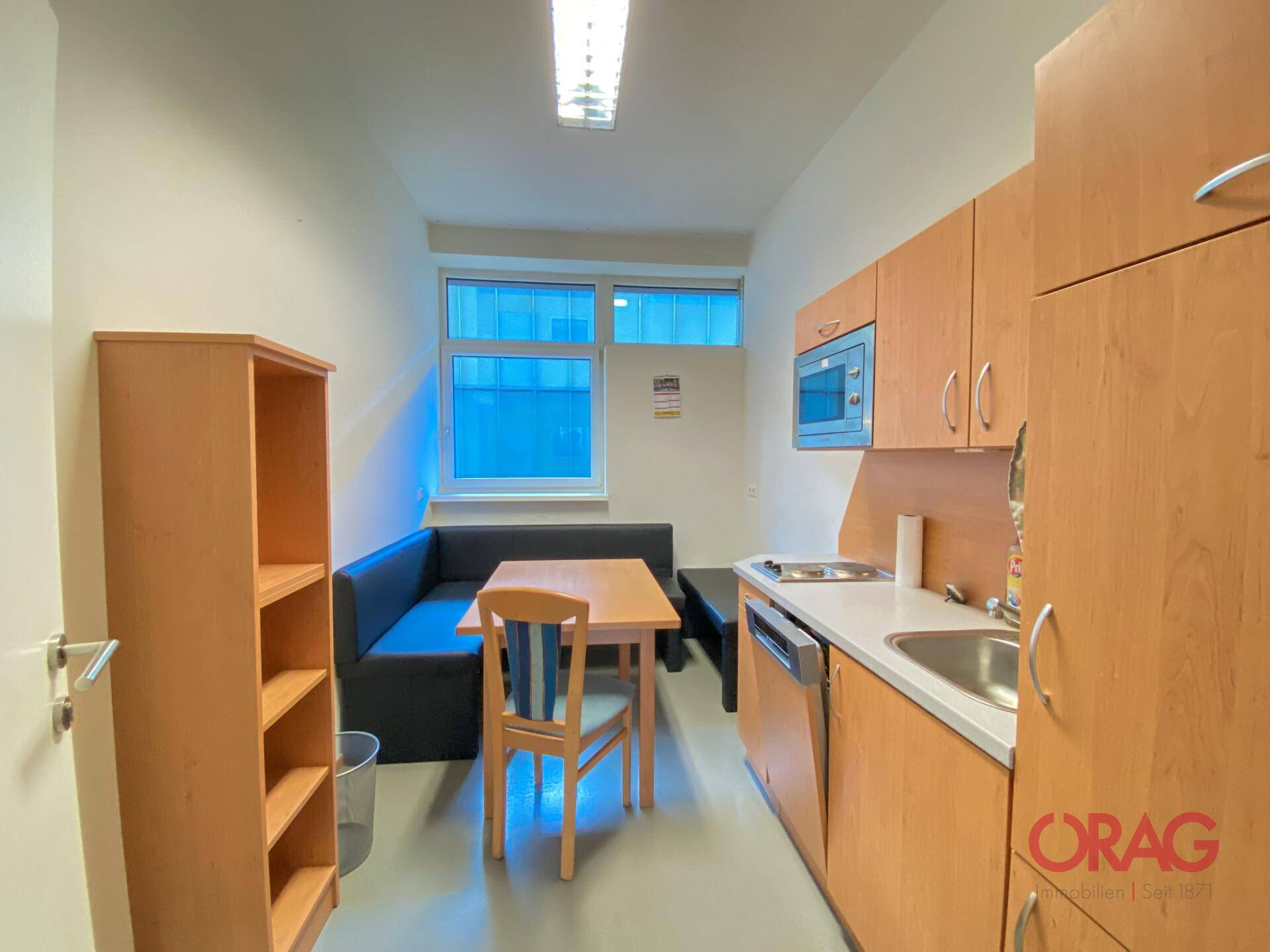Funktionale Küchenzeile mit Spüle, Mikrowelle und Essbereich, ideal für Pausen im Büro.