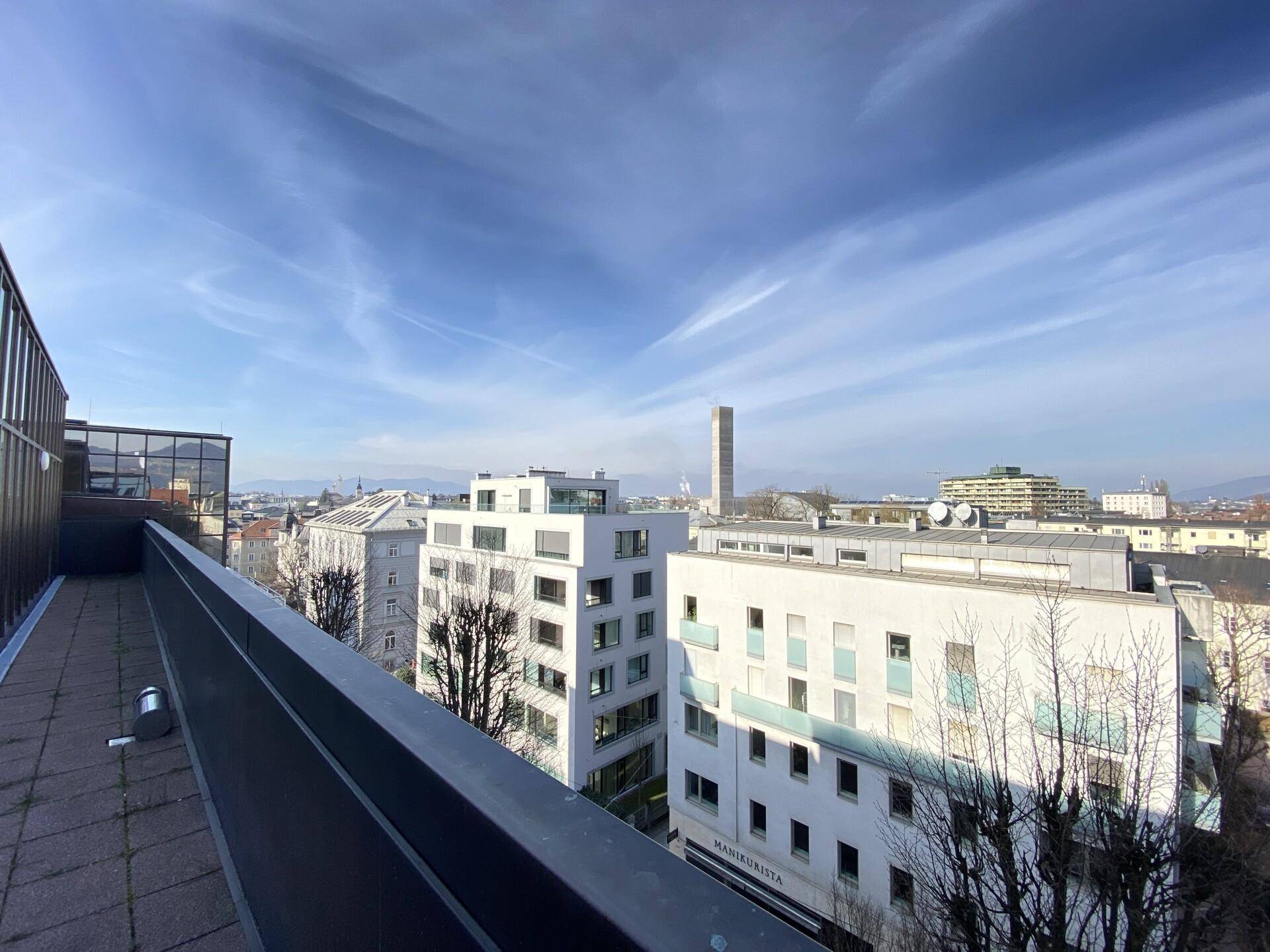 Weitläufiger Blick über die Stadt von einer Dachterrasse, mit modernen Gebäuden und blauem Himmel an einem sonnigen Tag.