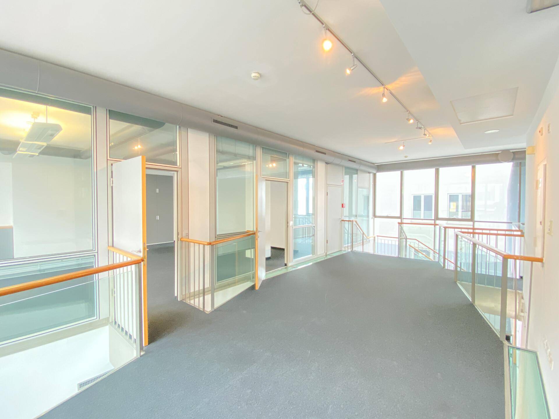 Offener Bürobereich auf einer oberen Etage mit Glasgeländern und Blick auf die darunterliegenden Räume.