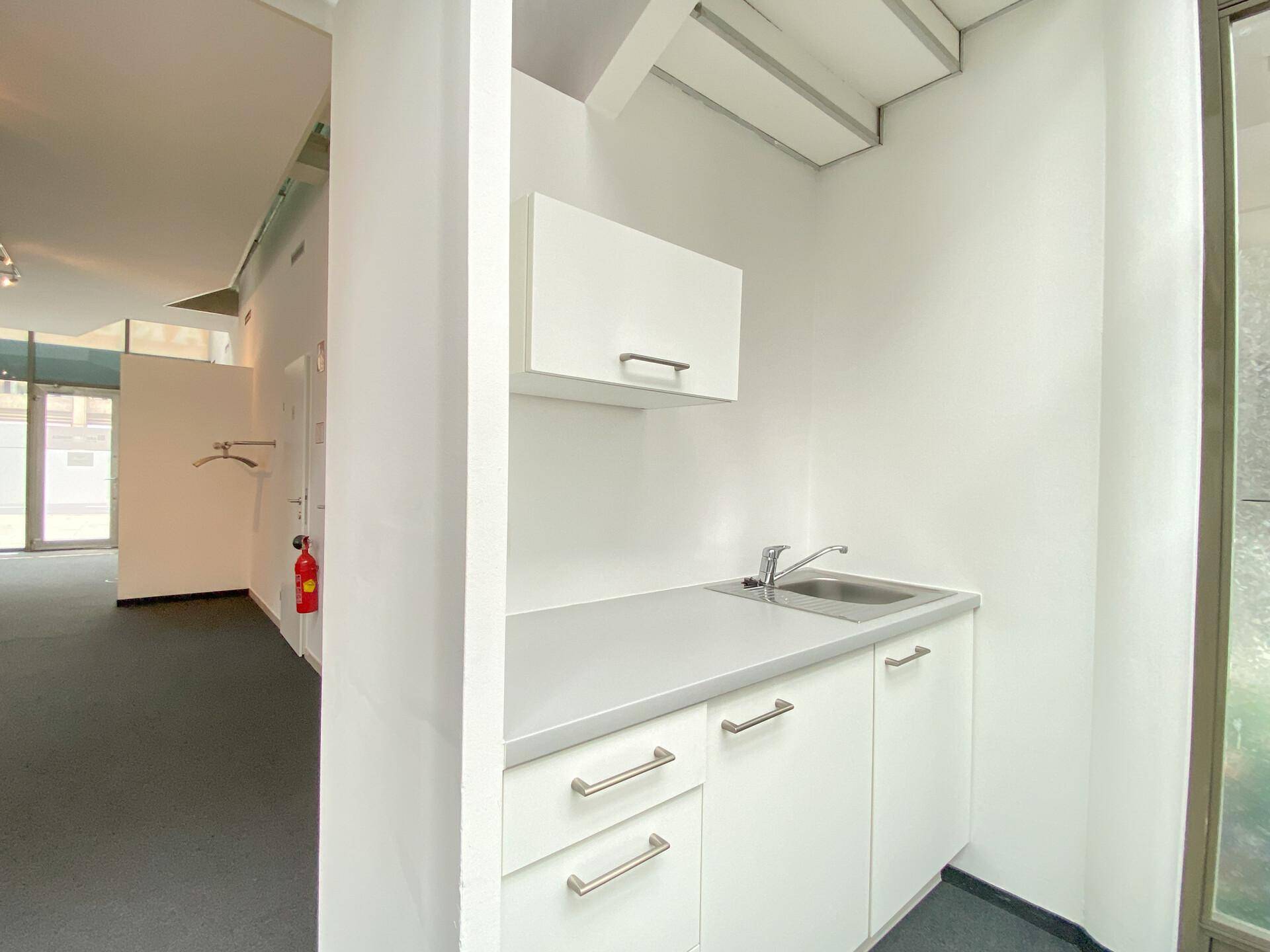 Einfache Küchenzeile mit Spülbecken, weißen Unterschränken und einer Arbeitsplatte in einem Bürobereich.