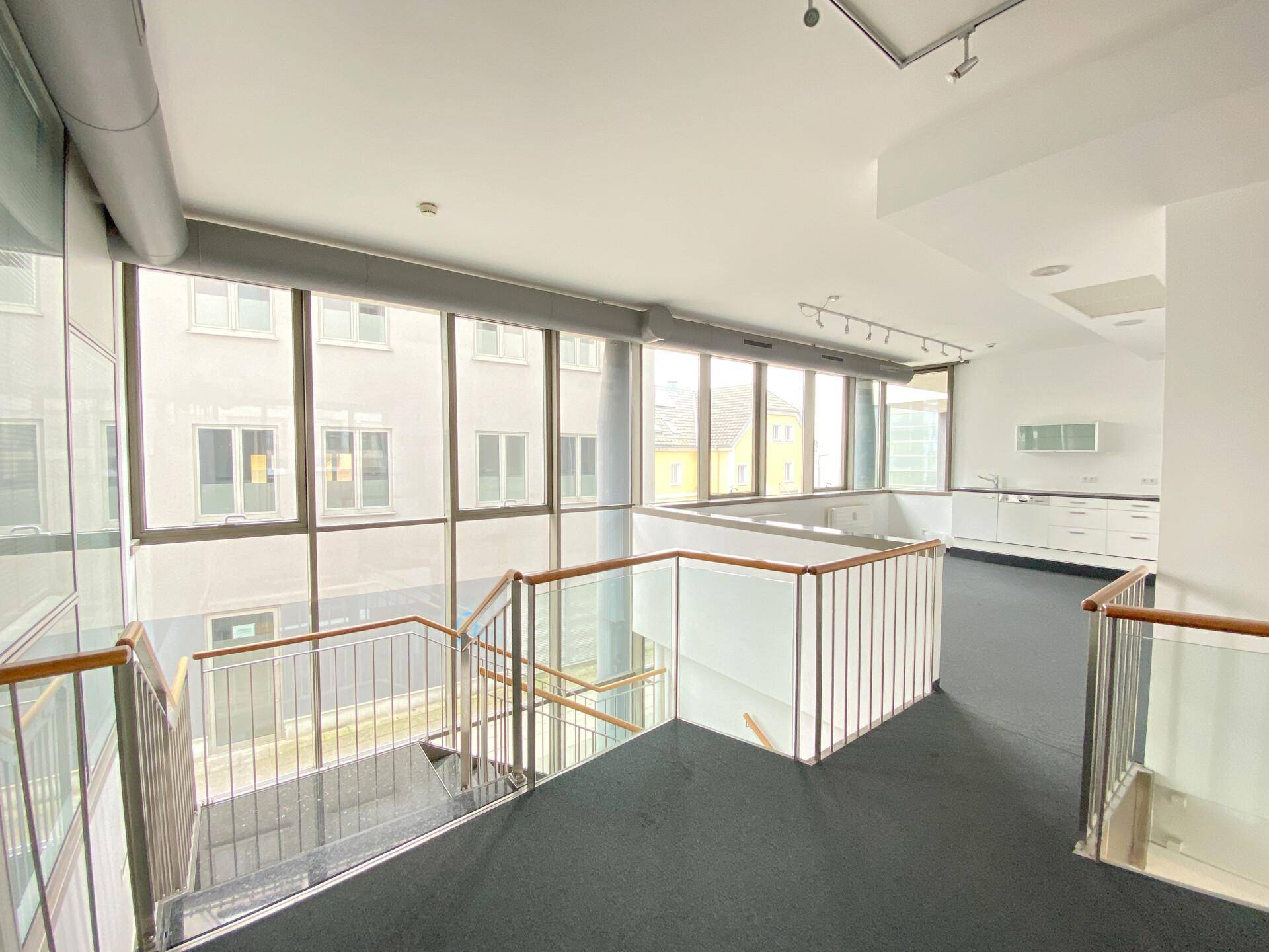 Heller Bürobereich auf einer oberen Ebene mit Blick auf die Treppe und eine kleine Küchenzeile.