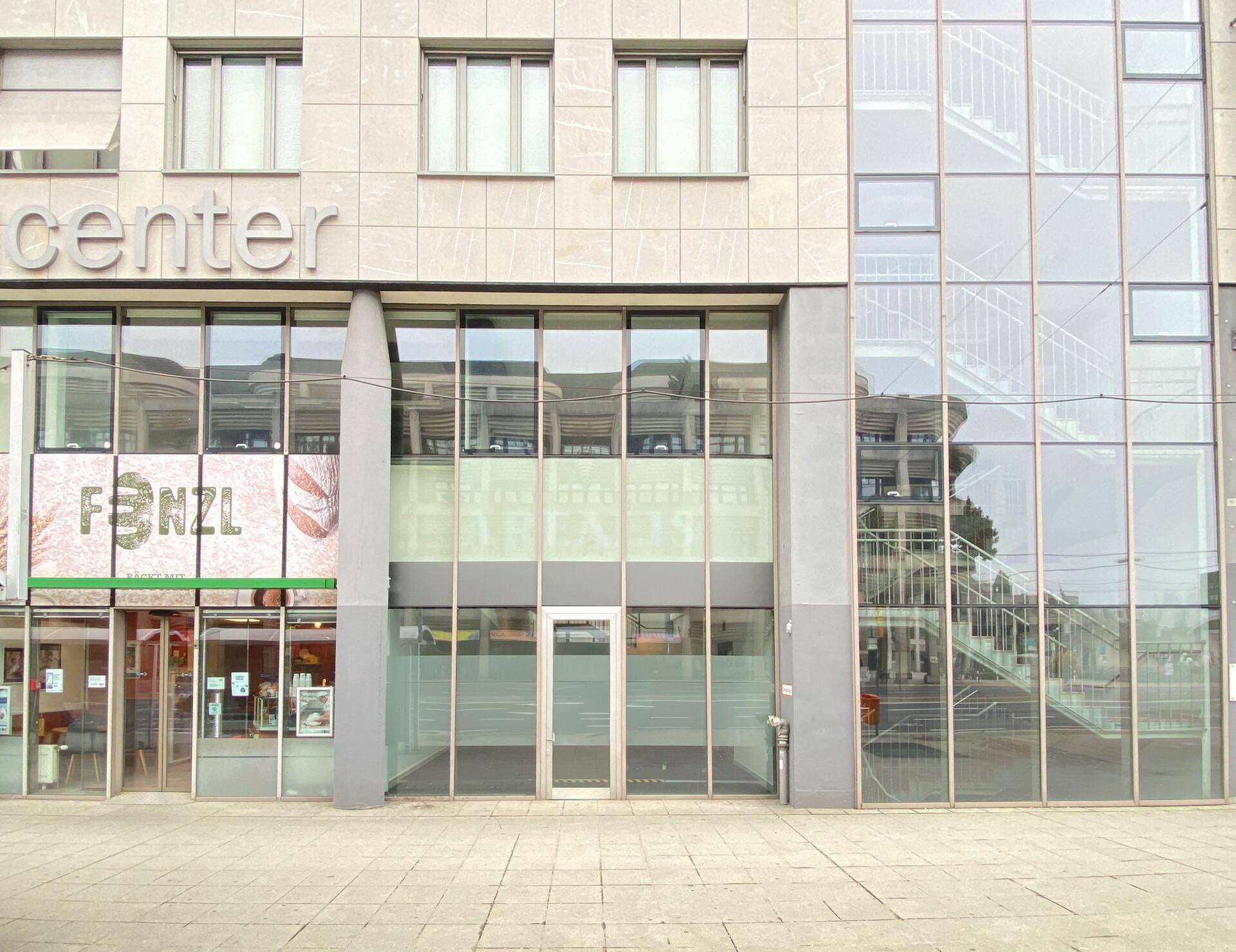Moderne Geschäftsfassade eines Einkaufszentrums mit großen Glasflächen und einem sichtbaren Treppenhaus.