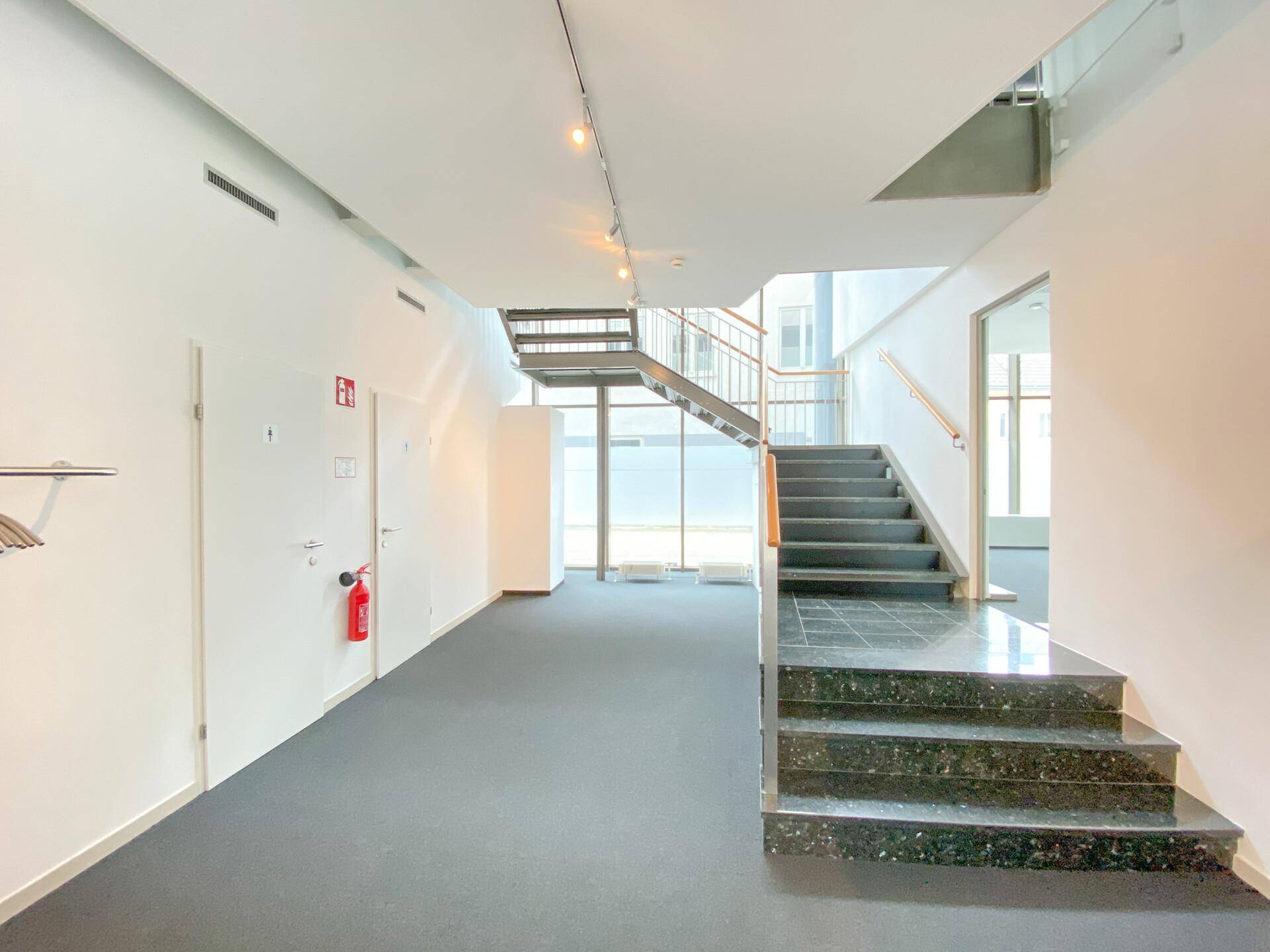 Geräumiger Flur mit Treppenaufgang, Teppichboden und modernen Glas- und Holzgeländern.