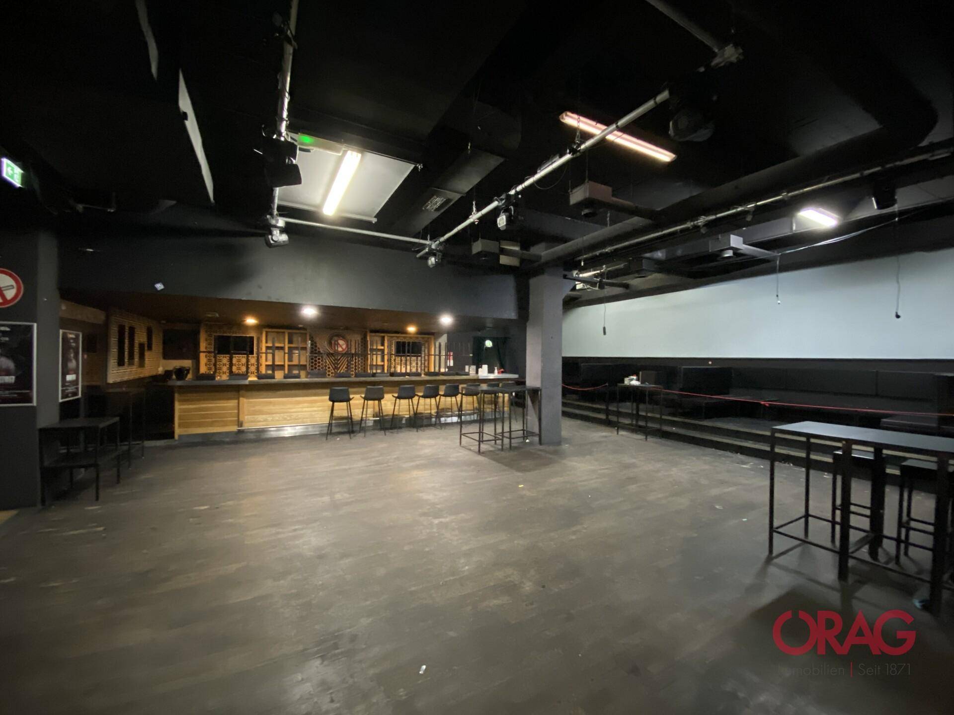 Weitläufiger Innenraum eines Clubs mit Bar, Sitzbereichen und dunklem Ambiente, ideal für Veranstaltungen.