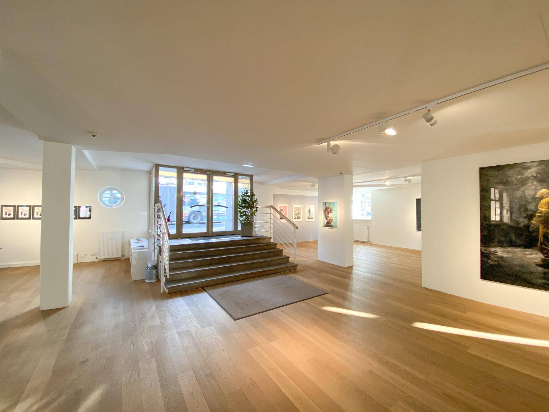Heller, offener Ausstellungsraum mit Holzboden, hohen Decken und Kunstwerken an den Wänden, einladend gestaltet.