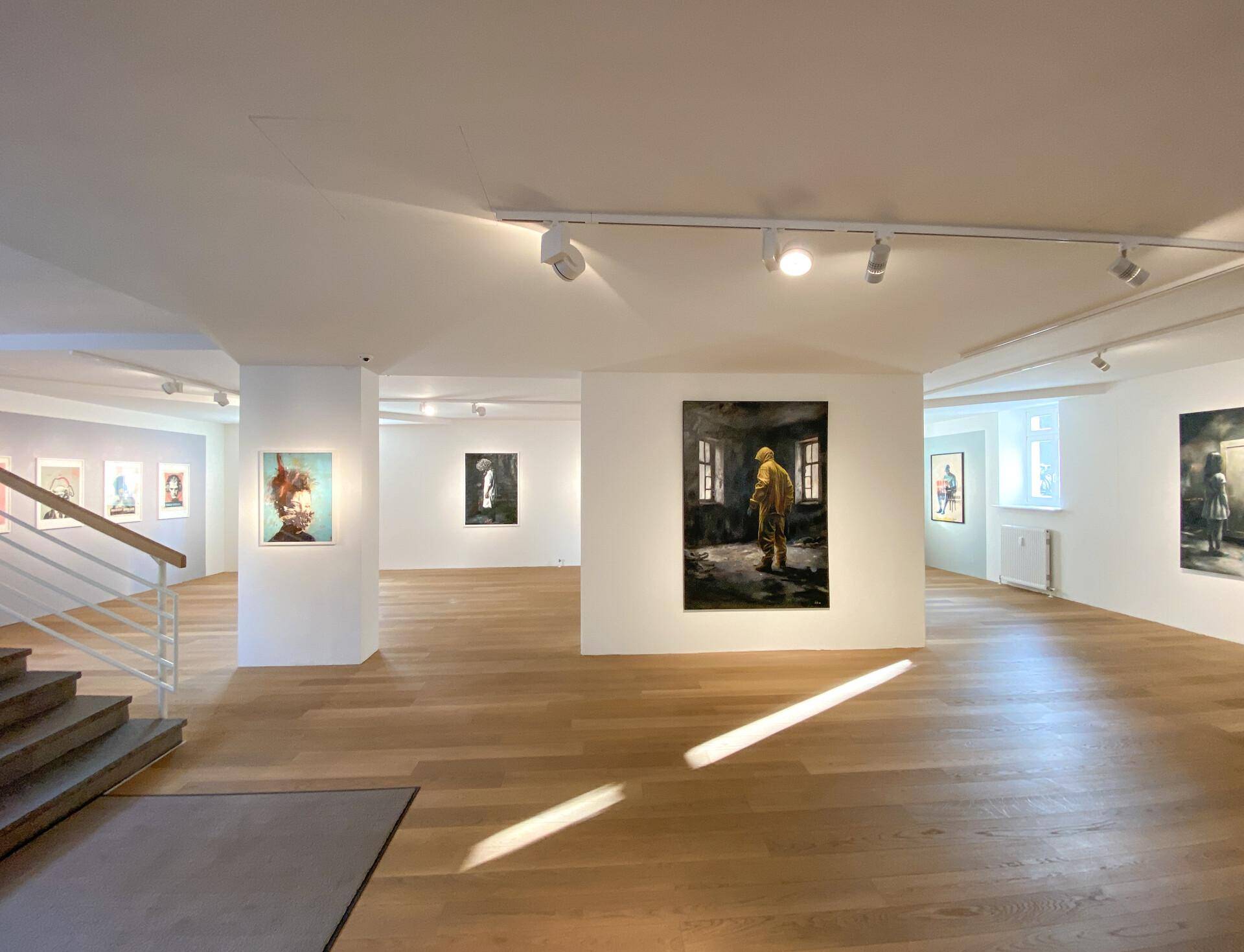 Geräumiger Ausstellungsbereich mit Holzboden, Kunstwerken und natürlichem Lichteinfall durch die großen Fenster.