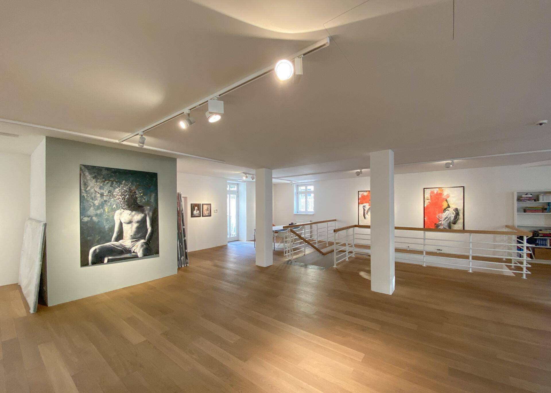 Heller Ausstellungsraum mit Holzboden, modernen Kunstwerken und einer Treppe zu einer weiteren Ebene.