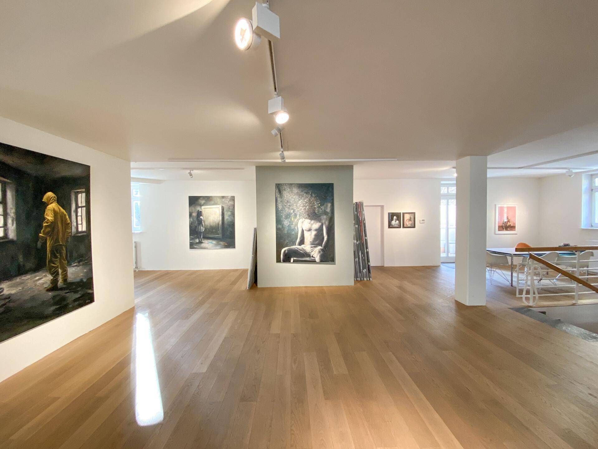 Weitläufiger Ausstellungsbereich mit Holzboden, verschiedenen Kunstwerken und viel Tageslicht durch die Fenster.