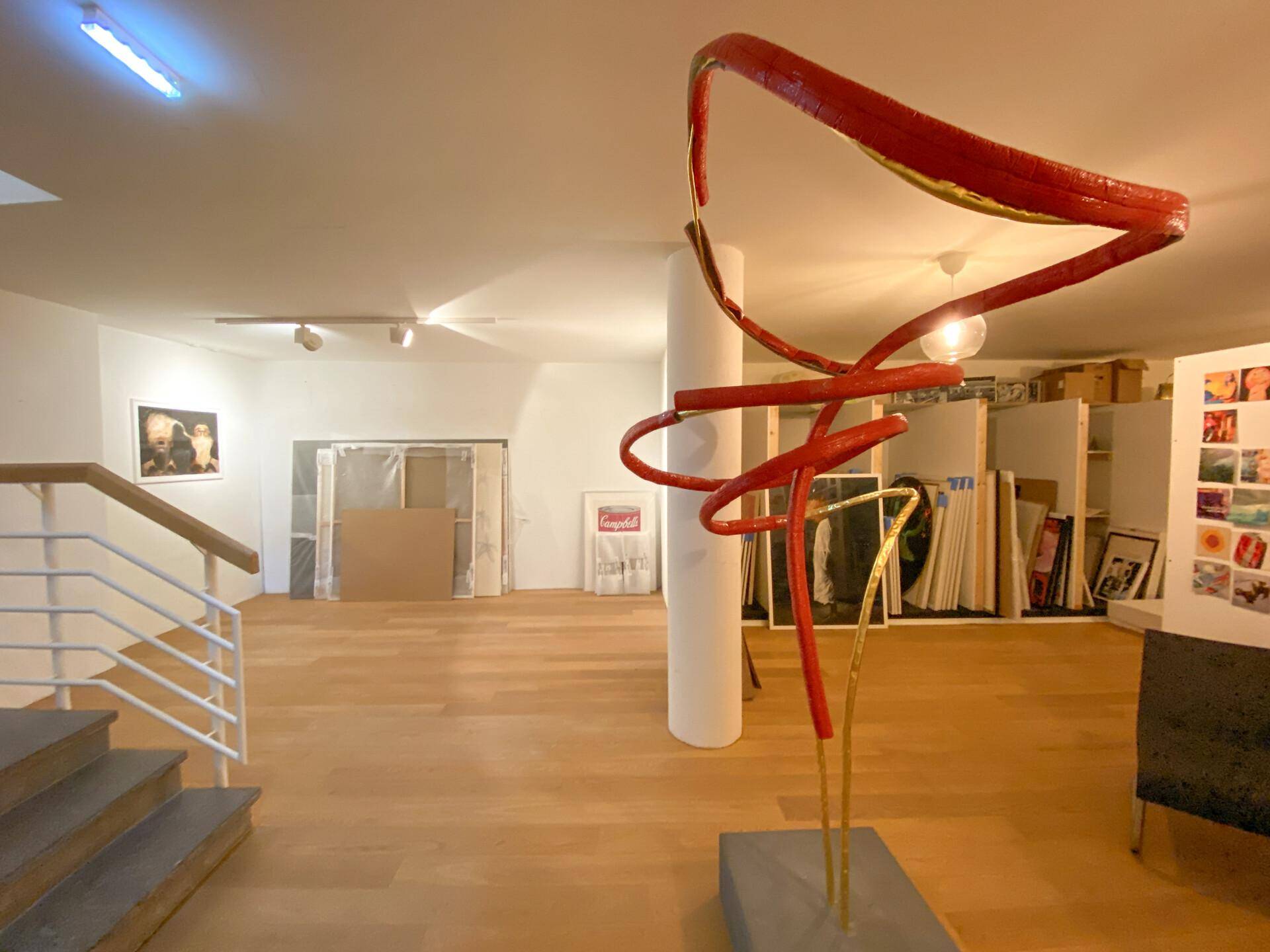 Lagerbereich oder Vorbereitungsraum der Galerie mit Kunstwerken, Verpackungsmaterialien und einer Treppe.