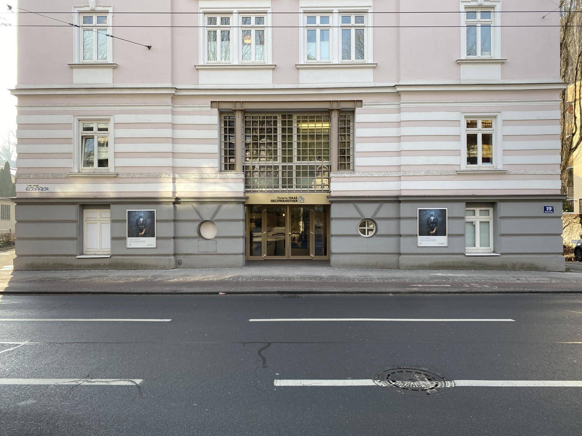 Historische Fassade eines Gebäudes mit großen Fenstern und einem Eingangsbereich an einer Straße.