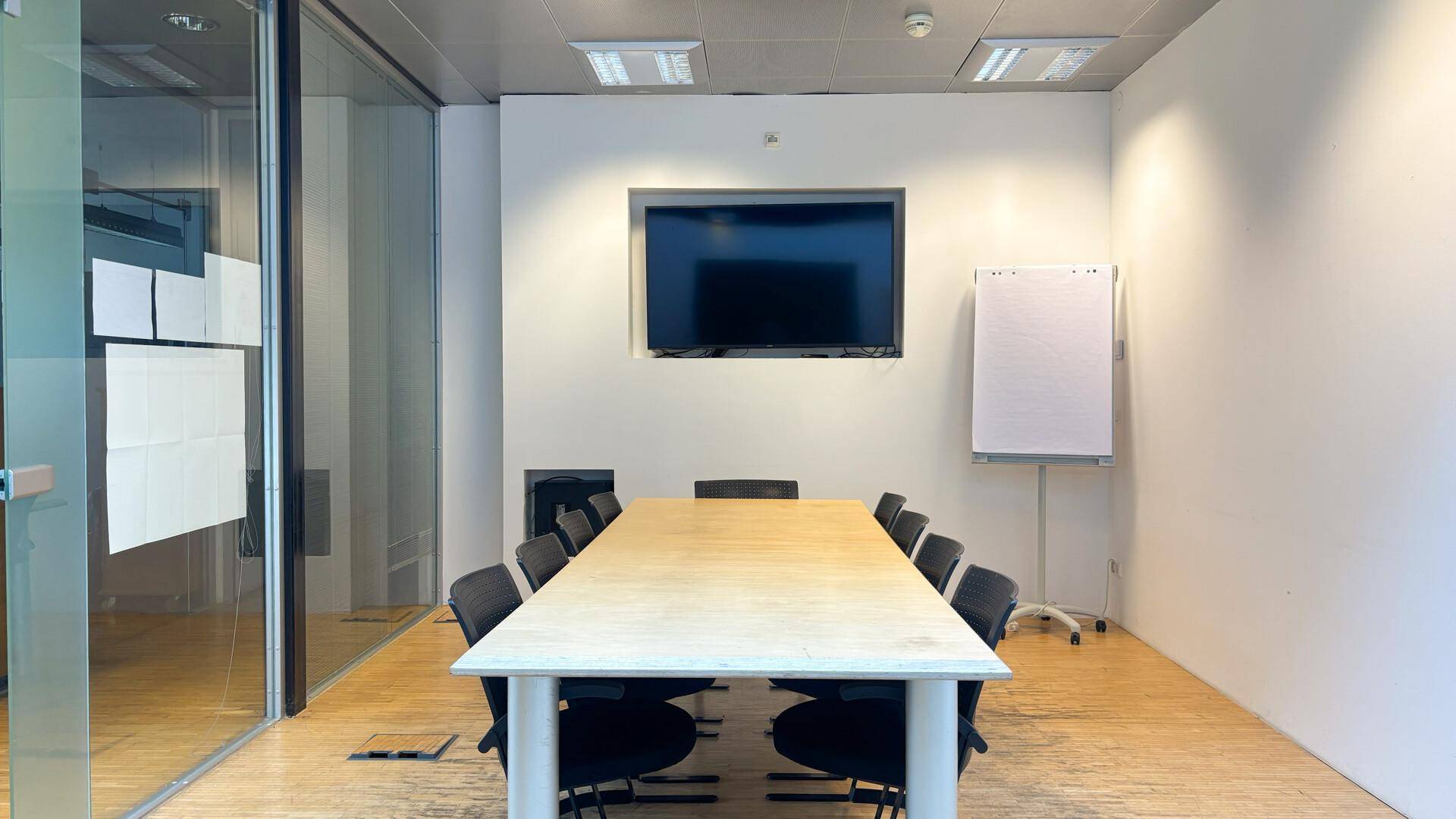 Moderner Konferenzraum mit großem Tisch, Stühlen und Wandfernseher für Präsentationen und Besprechungen.