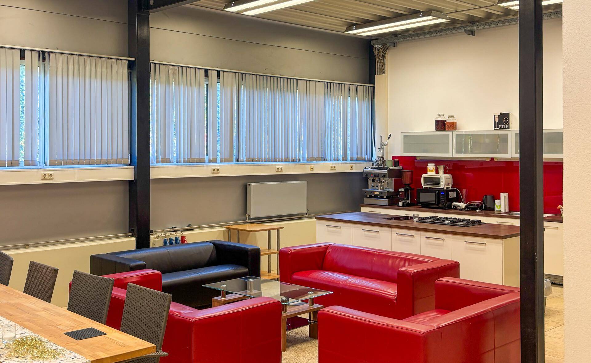 Gemütlicher Aufenthaltsraum mit roten Sofas, Esstisch und integrierter Küchenzeile für Pausen.
