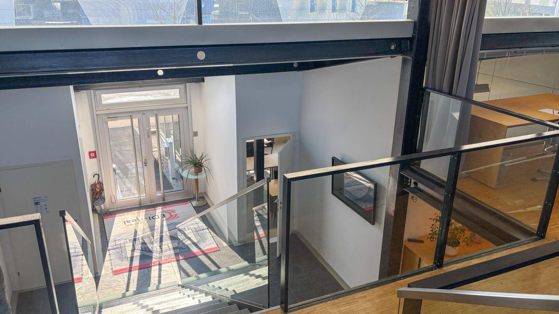 Heller Eingangsbereich mit moderner Treppe, Glasgeländer und Zugang zu den oberen Etagen.
