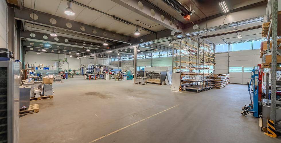 Weitläufige Lagerhalle mit hohen Regalen, Betonboden und großen Rolltoren, die viel Tageslicht hereinlassen.