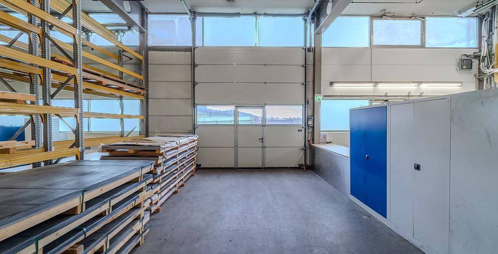 Großes Rolltor mit integrierter Zugangstür und Fensterfronten, umgeben von Lagerregalen und Schränken in einer Halle.