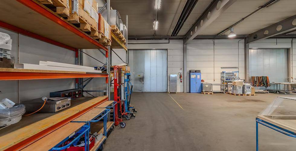 Geräumige Lagerhalle mit hohen Decken, Betonboden und einem großen Tor im Hintergrund, bereit für den Betrieb.