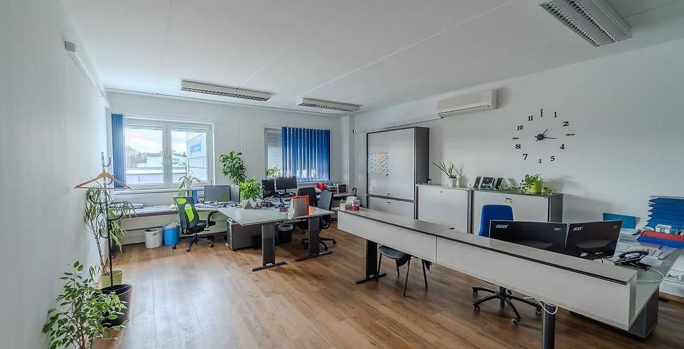 Geräumiges Büro mit mehreren Arbeitsplätzen, Holzfußboden und Klimaanlage, hell und funktional eingerichtet.