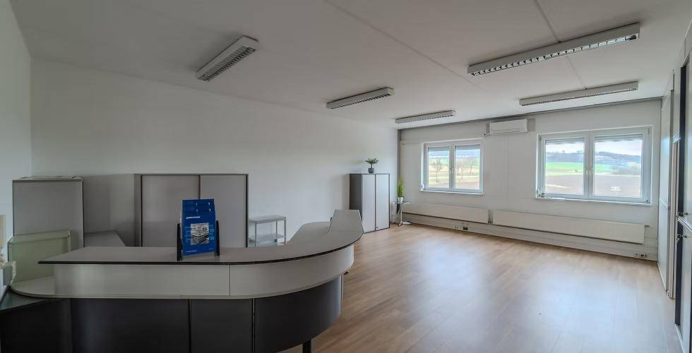 Großer Empfangsbereich mit geschwungenem Tresen, Holzfußboden und Fenstern, die viel Licht hereinlassen.
