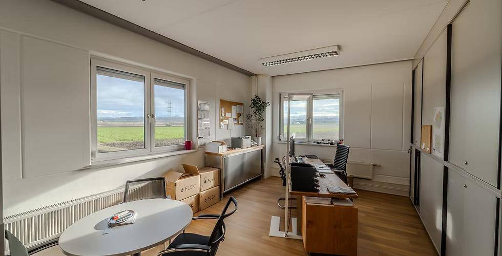 Funktionales Büro mit zwei Arbeitsbereichen, Holzfußboden und Fenstern mit Blick auf die umliegende Landschaft.