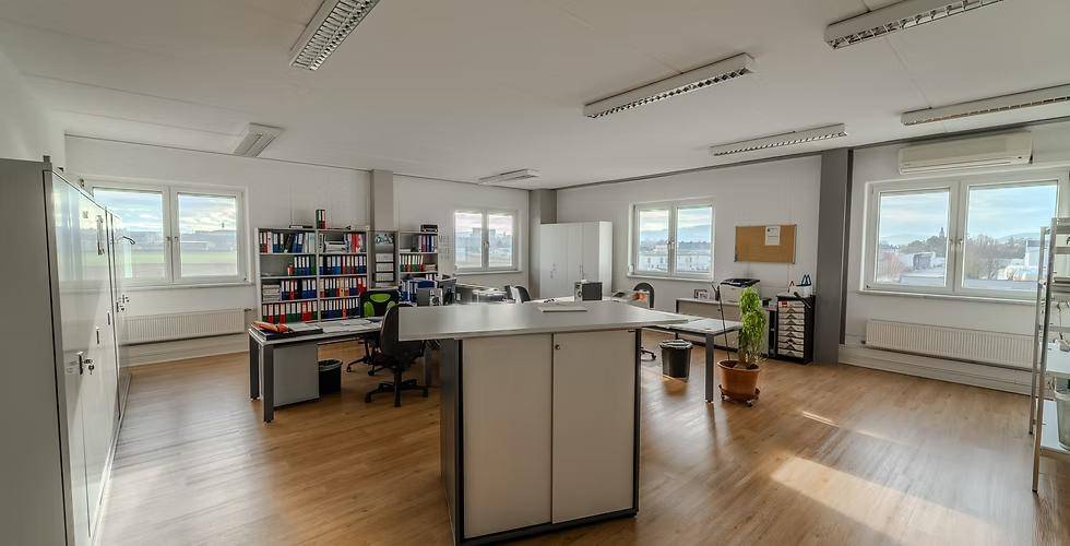 Großes, helles Büro mit mehreren Arbeitsplätzen, Holzfußboden und Fenstern, die eine weite Aussicht bieten.