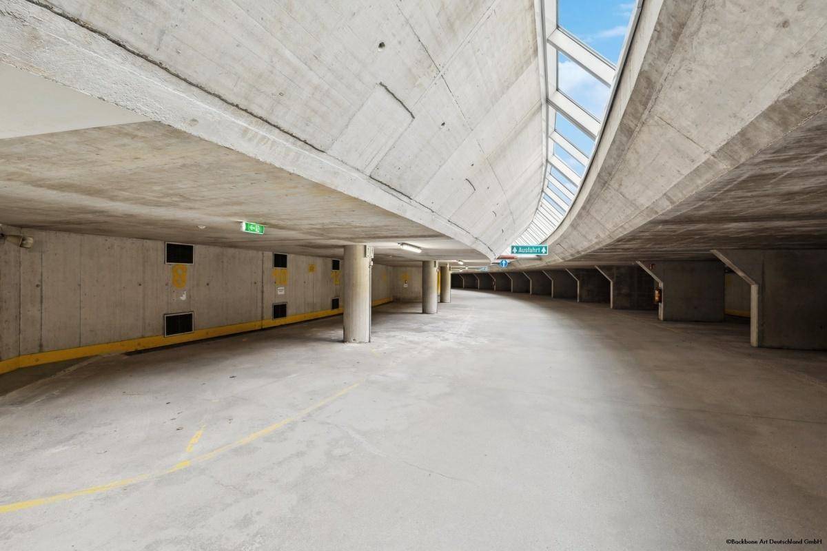 Geräumige Tiefgarage mit Betonwänden und -decken, gut beleuchtet und mit natürlichem Lichteinfall von oben.