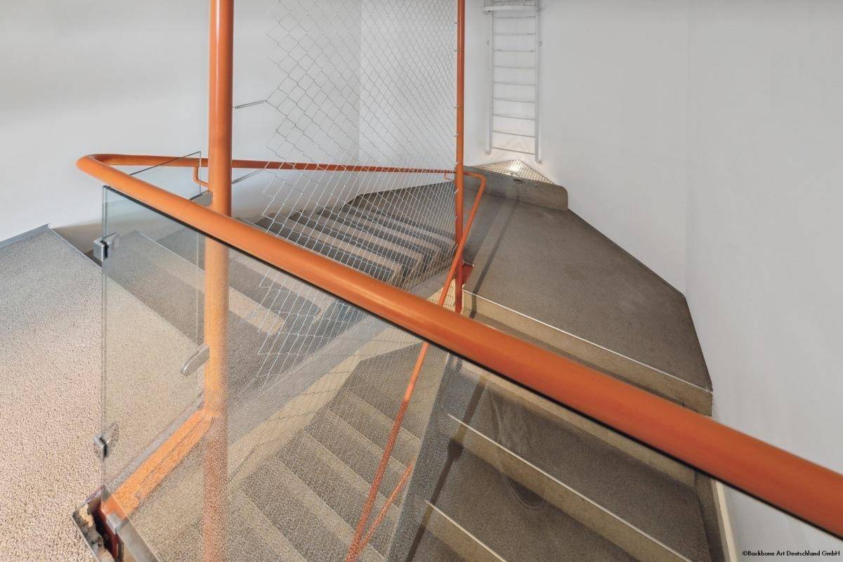 Modernes Treppenhaus mit orangefarbenen Handläufen, Glasgeländer und Betonstufen.