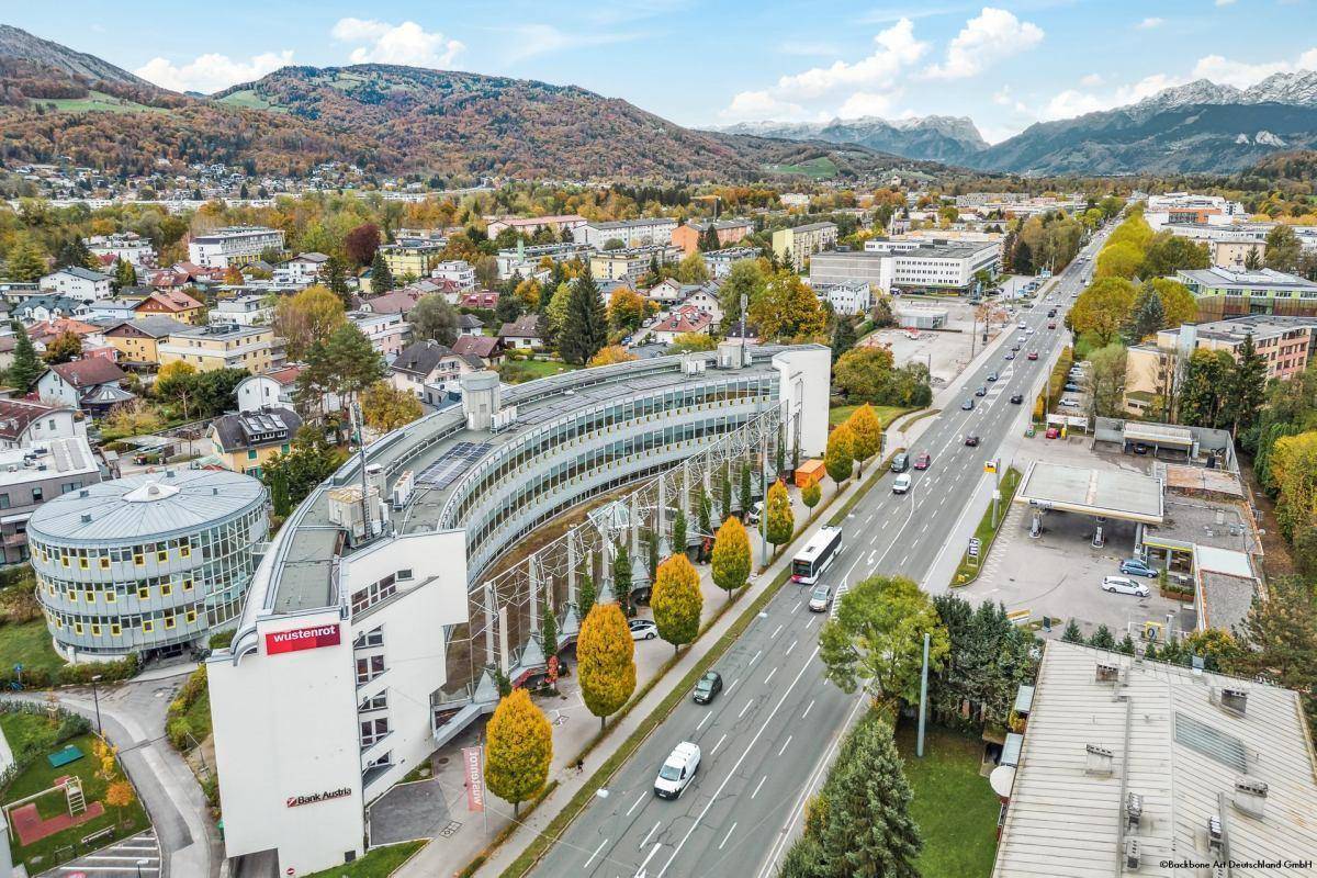 Luftaufnahme des Bürogebäudes entlang einer Hauptstraße, umgeben von Wohngebieten und grünen Hügeln.