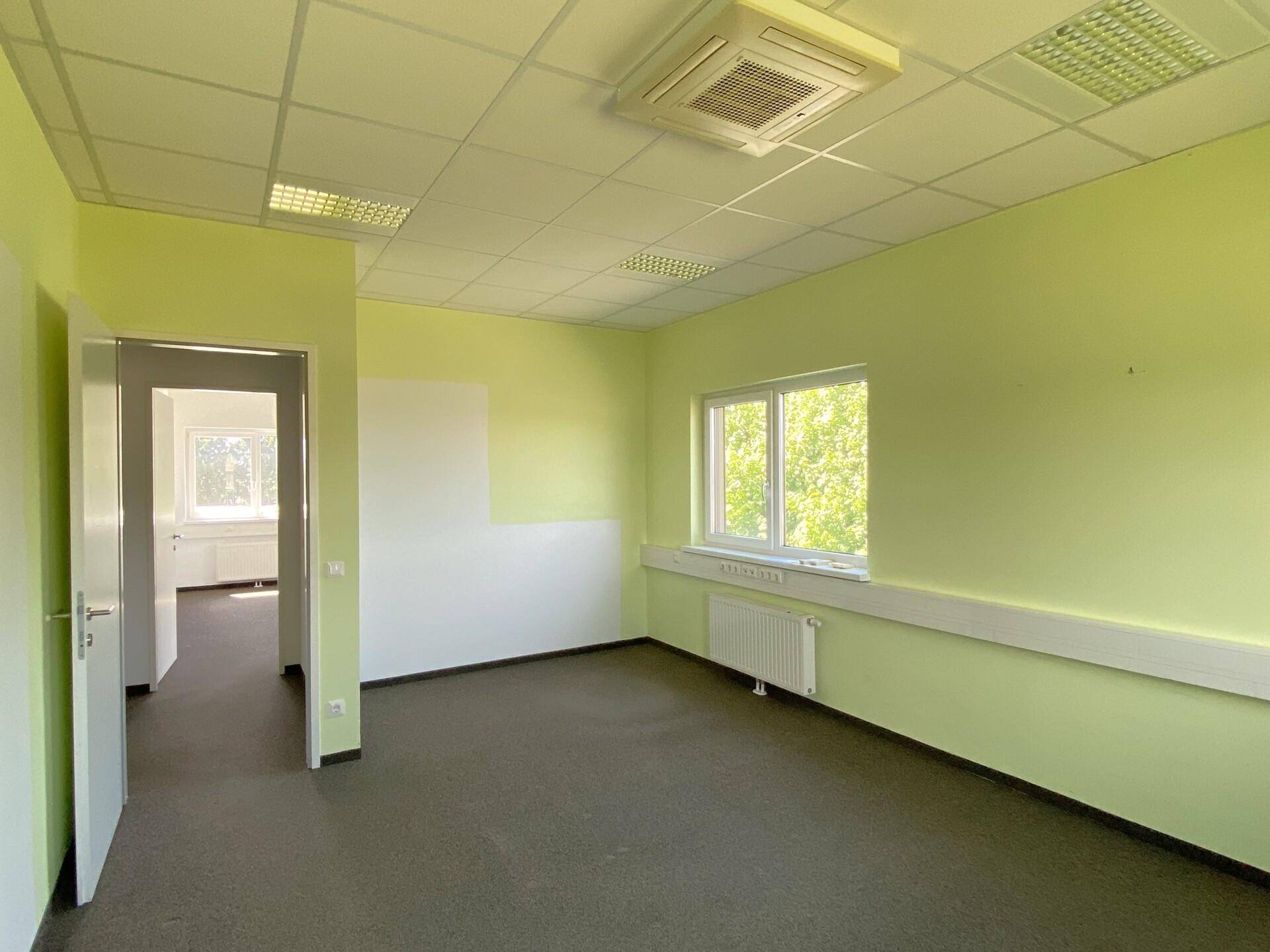 Büro mit grünen Akzentwänden, Teppichboden und Klimaanlage, mit Zugang zu einem weiteren Raum.