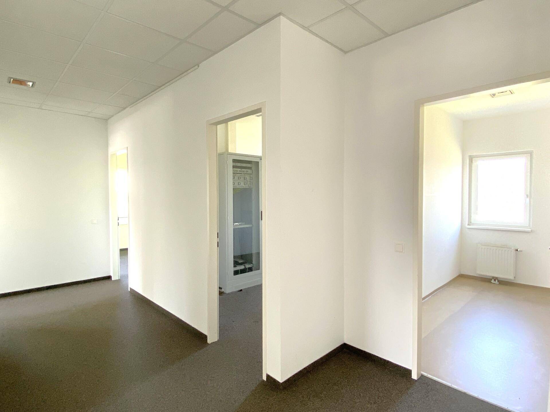 Heller Flur mit weißen Wänden und dunklem Bodenbelag, verbindet mehrere Büroräume miteinander.