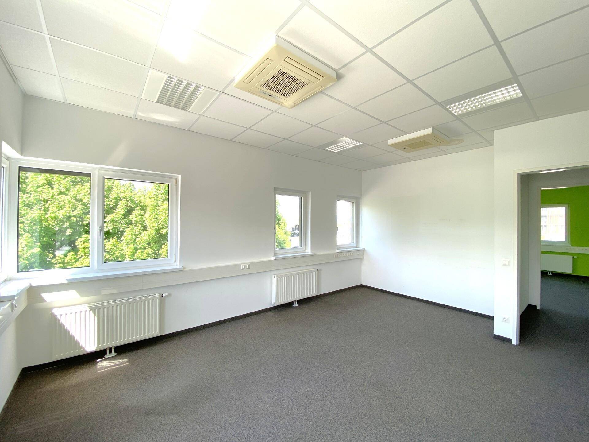 Geräumiges Büro mit Teppichboden, Klimaanlage und Blick ins Grüne, angrenzend an einen weiteren Raum.