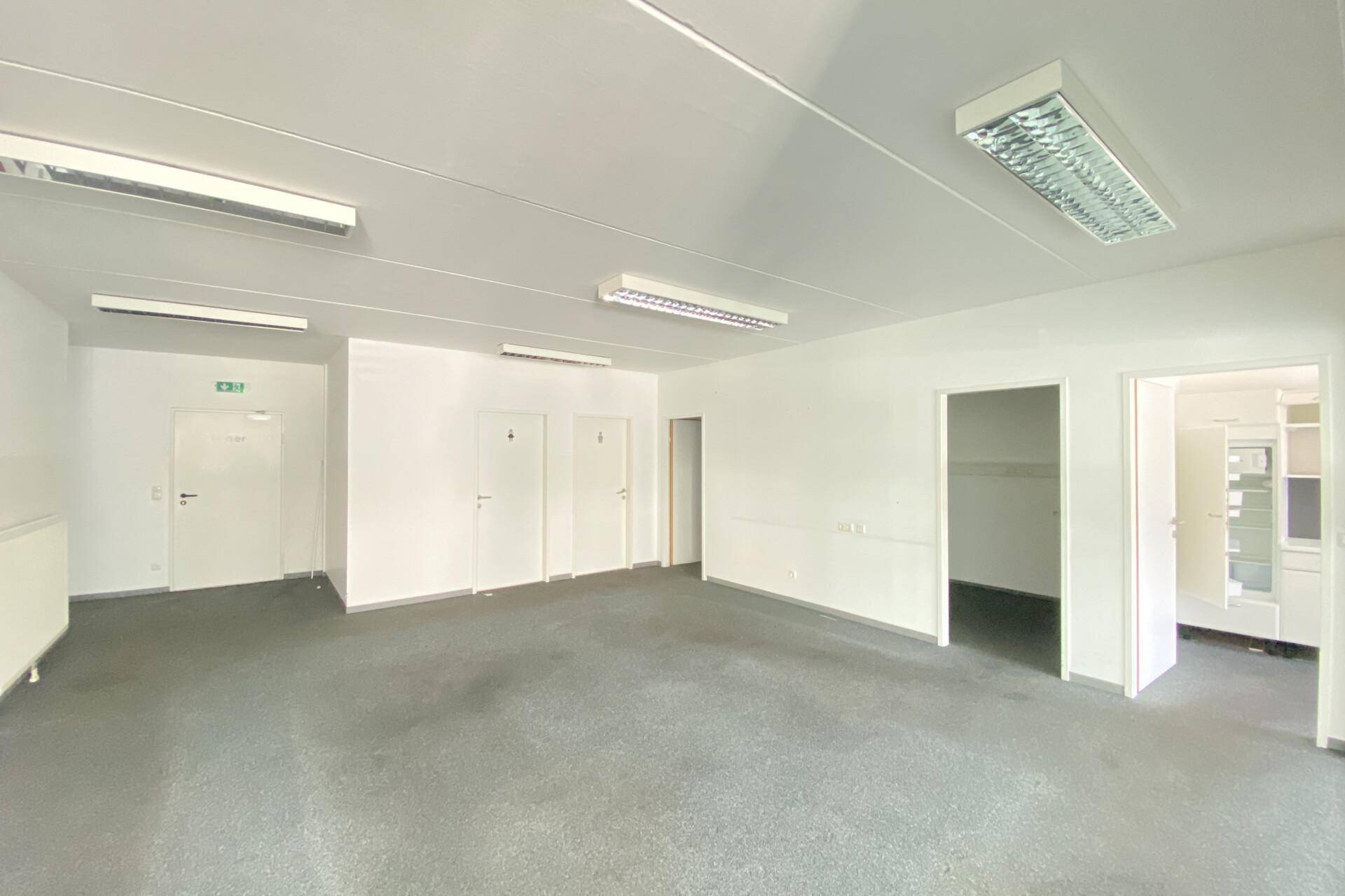Großer, offener Bürobereich mit Teppichboden, mehreren Türen und effizienter Deckenbeleuchtung.