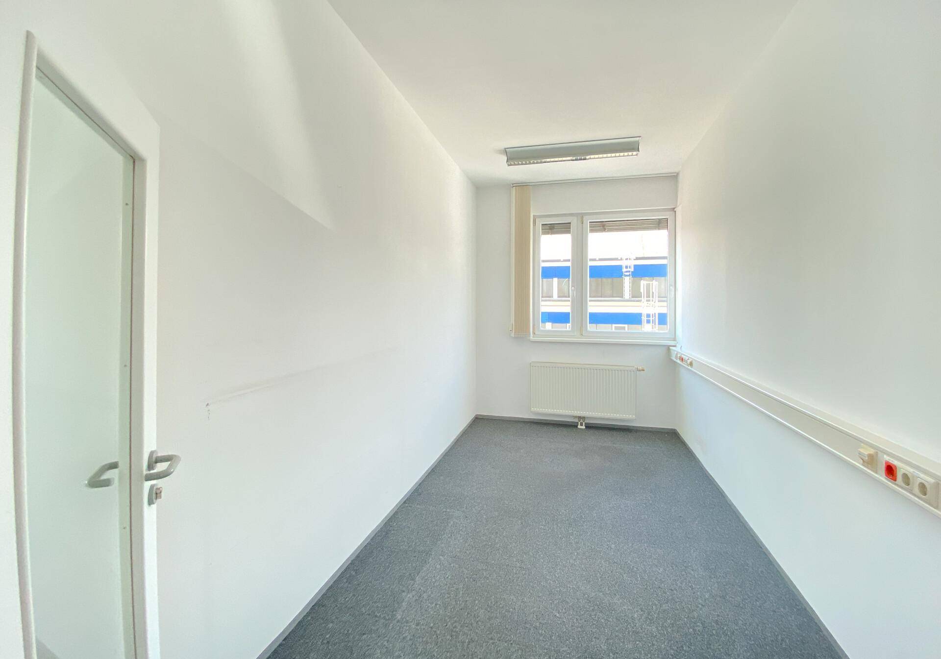 Langes, schmales Büro mit Teppichboden, Fenster, Heizkörper und einer modernen Glastür.