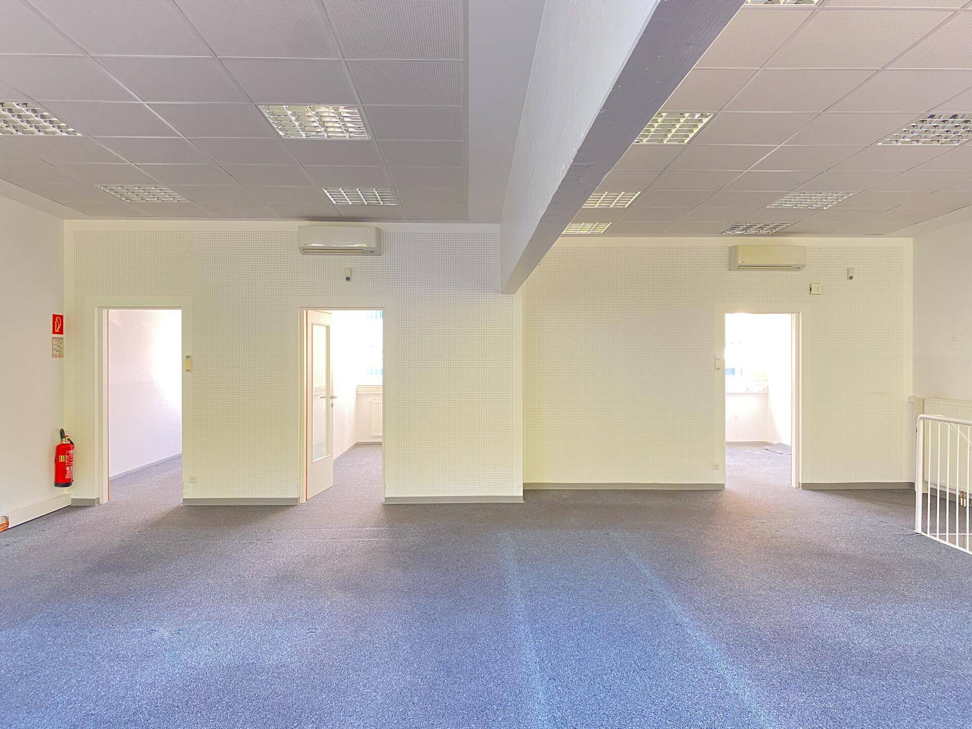 Heller, offener Bürobereich mit Teppichboden, Klimaanlage und moderner Deckenbeleuchtung.