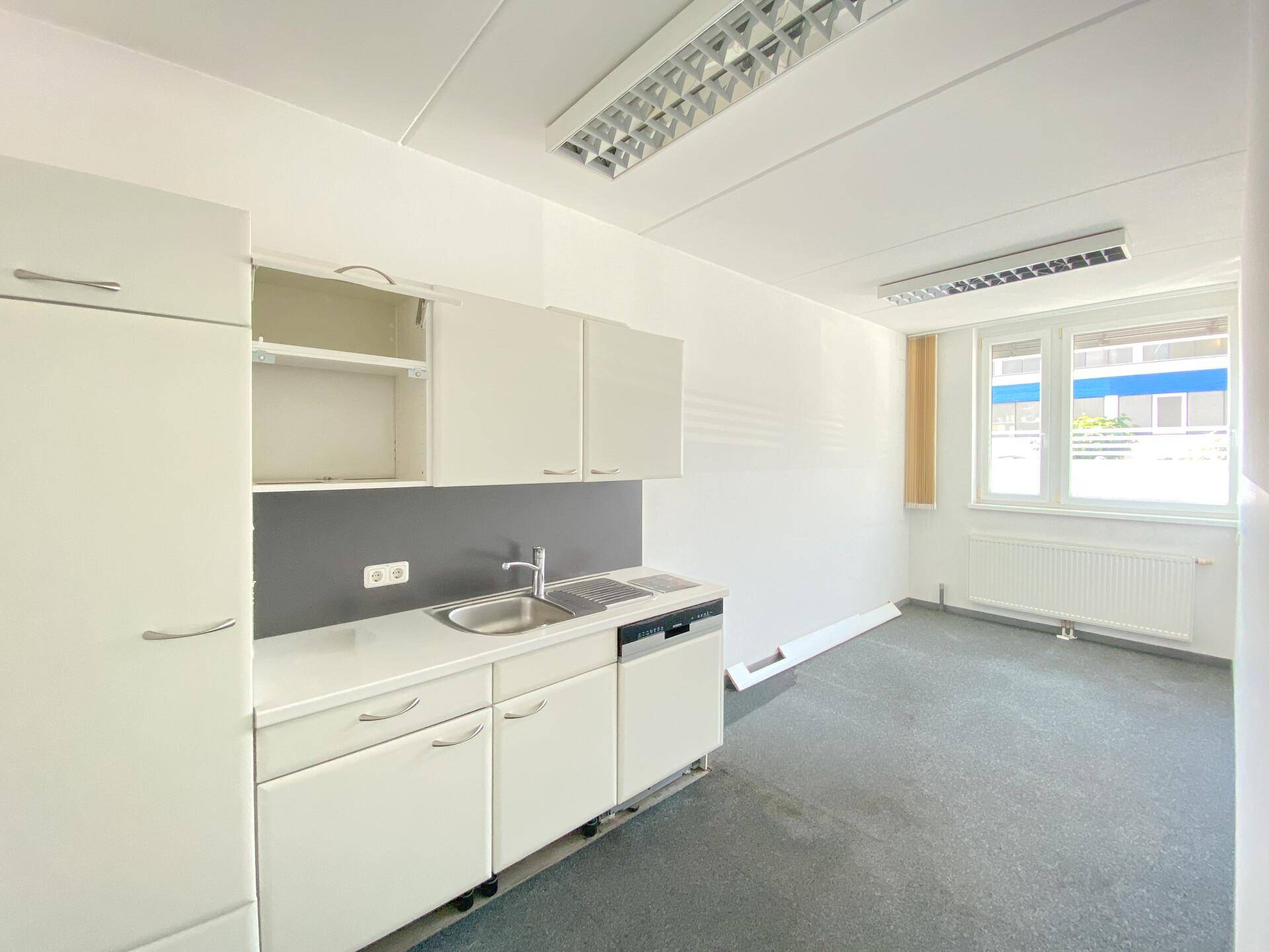 Funktionale Küchenzeile mit weißen Schränken, Spüle, Kochfeld und Geschirrspüler in einem Büroraum.