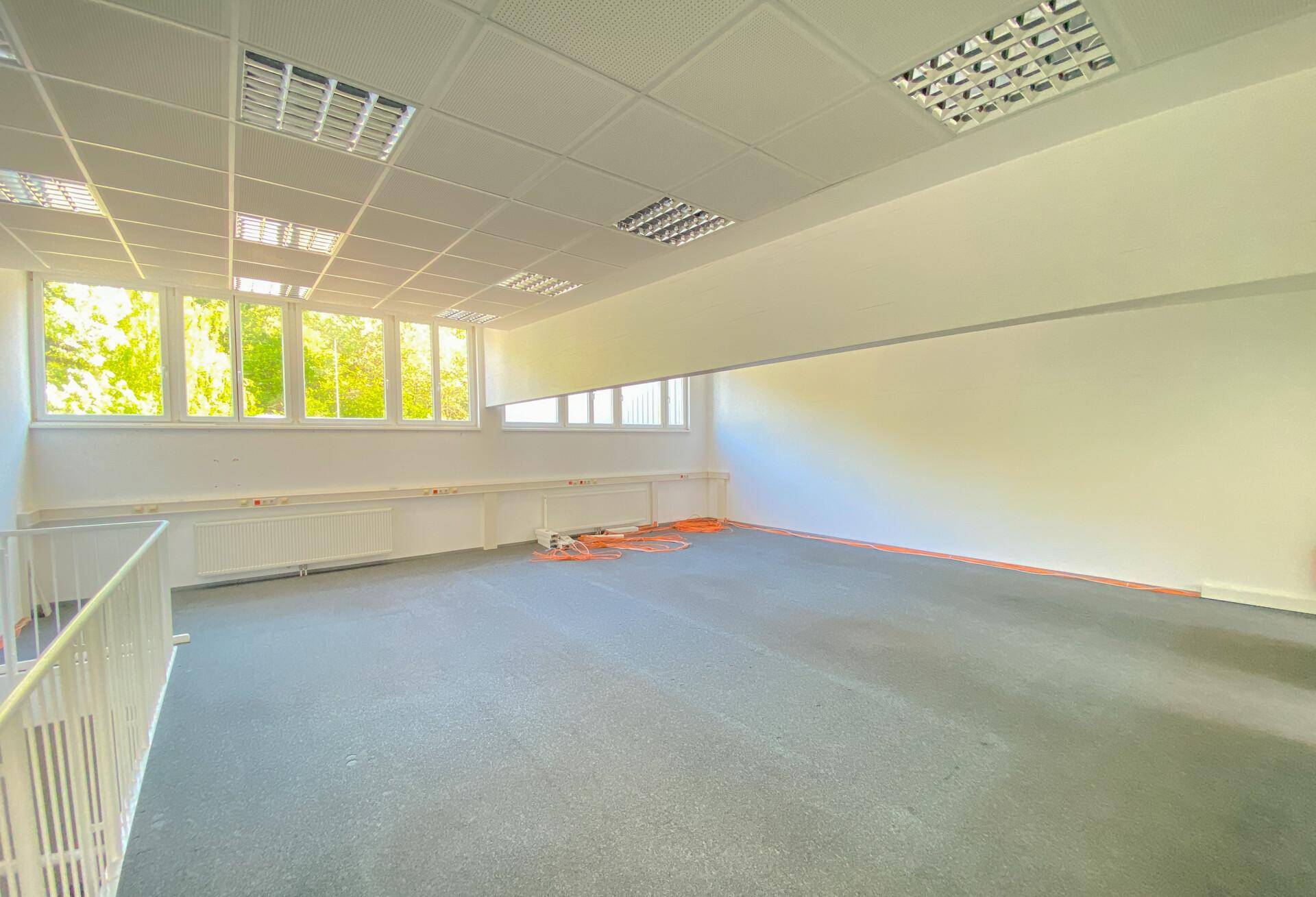 Geräumiger Bürobereich mit Teppichboden, großen Fenstern und vorbereiteten Kabeln für Installationen.