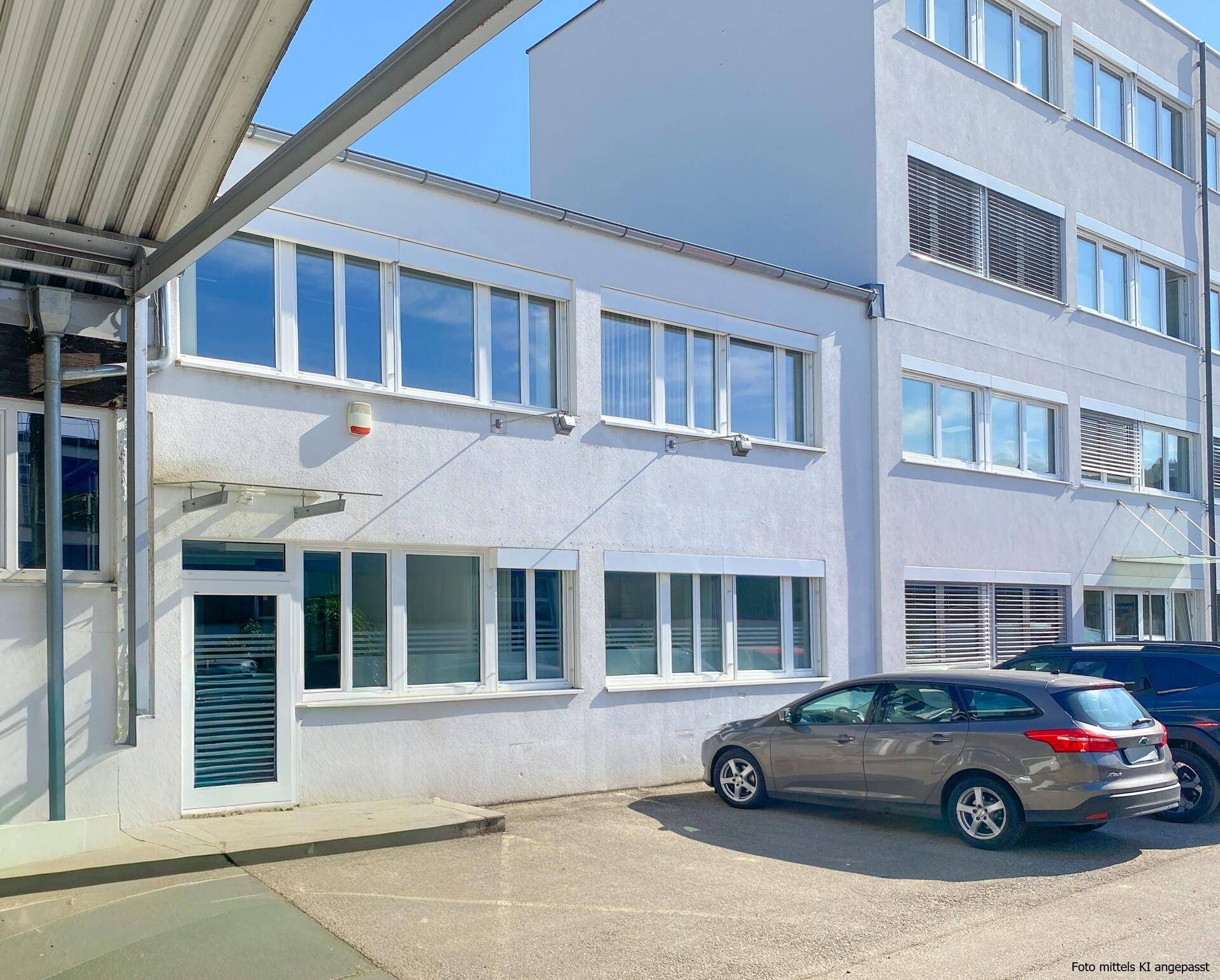 Modernes Geschäftsgebäude mit grauer Fassade, vielen Fenstern und geparkten Autos davor.