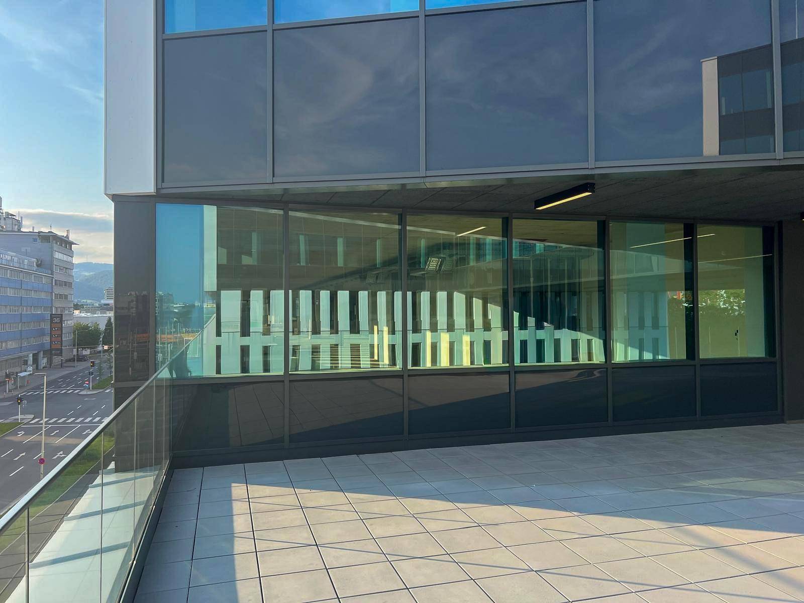 Eine geräumige Terrasse mit Glasgeländer und Blick auf die moderne Glasfassade des Gebäudes.