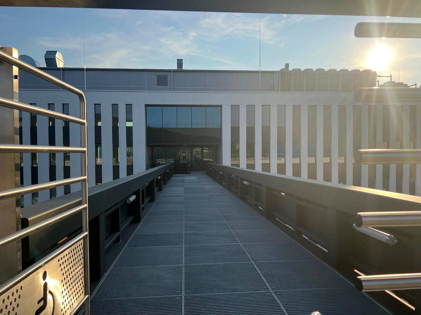 Eine barrierefreie Rampe mit Metallgeländer führt zu einem modernen Gebäudeeingang im Sonnenlicht.