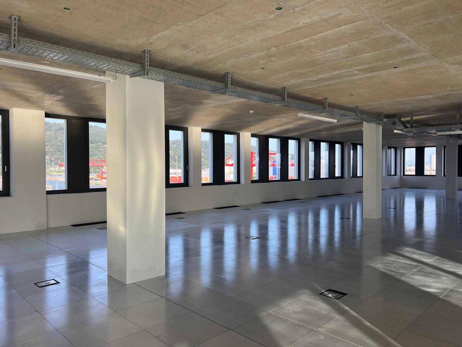 Weitläufiger Büroraum mit Reihen von Fenstern und sichtbaren Kabeltrassen an der Betondecke.