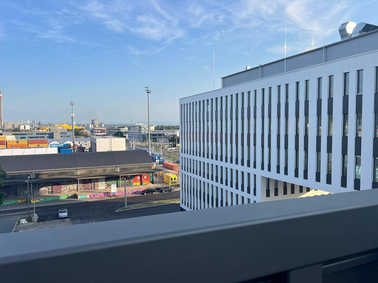 Blick von einem Balkon auf ein Industriegebiet mit Containern und einem modernen Bürogebäude.